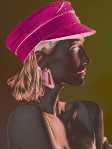 Emanuel Klempa, Fotograf München. Ein von der Modebranche inspiriertes, stilisiertes Porträt einer Frau im Profil, die einen hellrosa Hut und geometrische Ohrringe trägt, mit dramatischer Beleuchtung und kontrastreichen Farben, die ihre Gesichtszüge und Kleidung betonen.